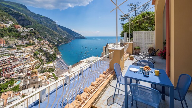 A terrace with a table and chairs overlooking a coastal town and the sea. - Casa Bijou (Positano)