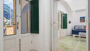 A hallway with white walls, green shutters, and a view of a coastal area. - Casa Bijou (Positano)