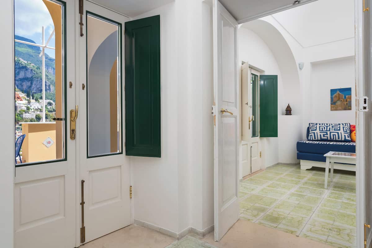 A hallway with white walls, green shutters, and a view of a coastal area.