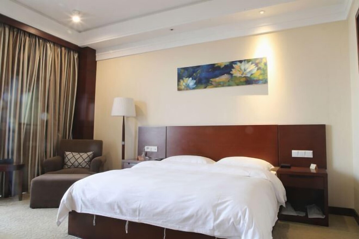 A hotel room with a large bed, a chair, a nightstand, a lamp, and a painting on the wall.