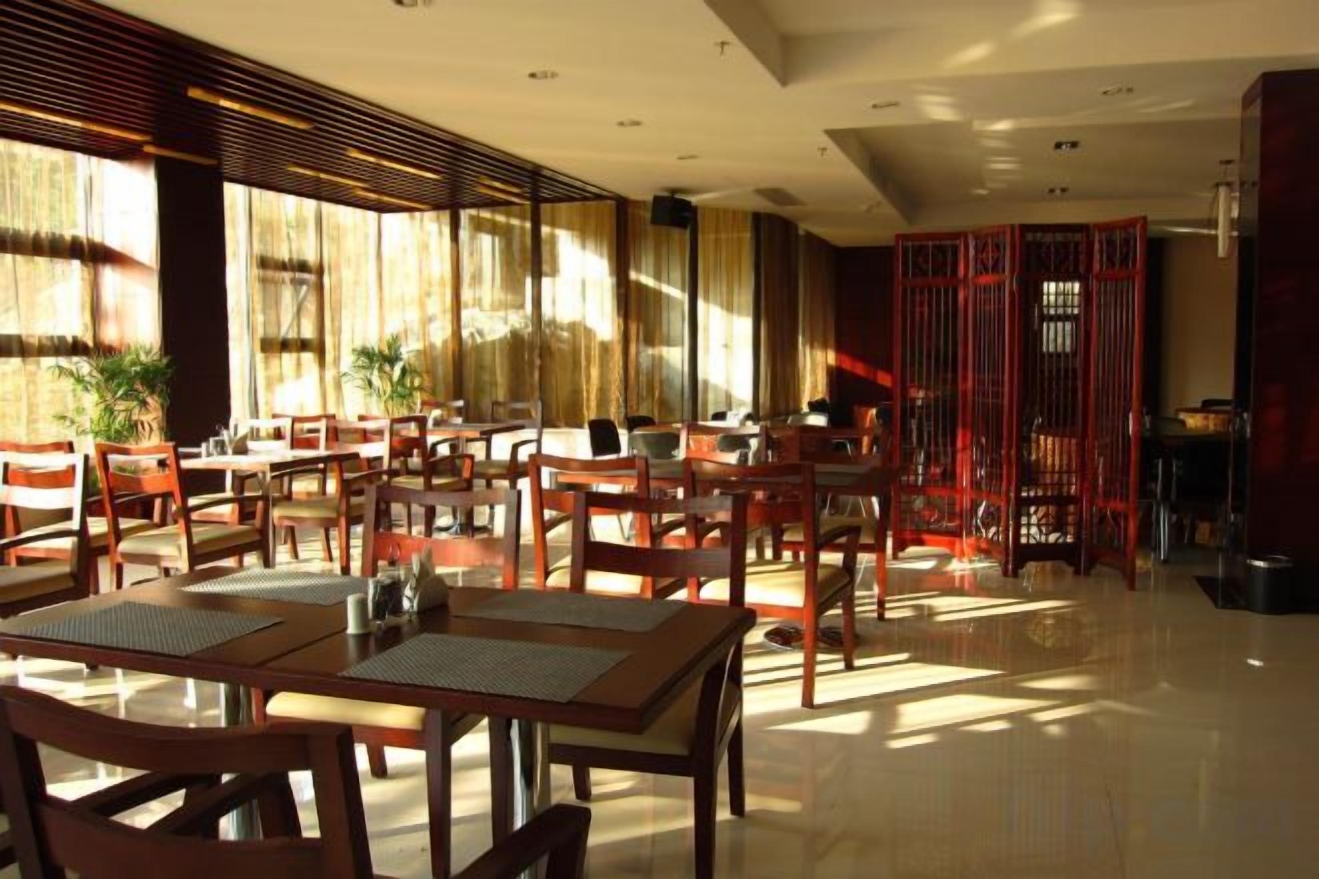 A spacious dining area with multiple tables and chairs, large windows allowing natural light, and a traditional red partition in the background.