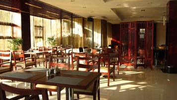 A spacious dining area with multiple tables and chairs, large windows allowing natural light, and a traditional red partition in the background.