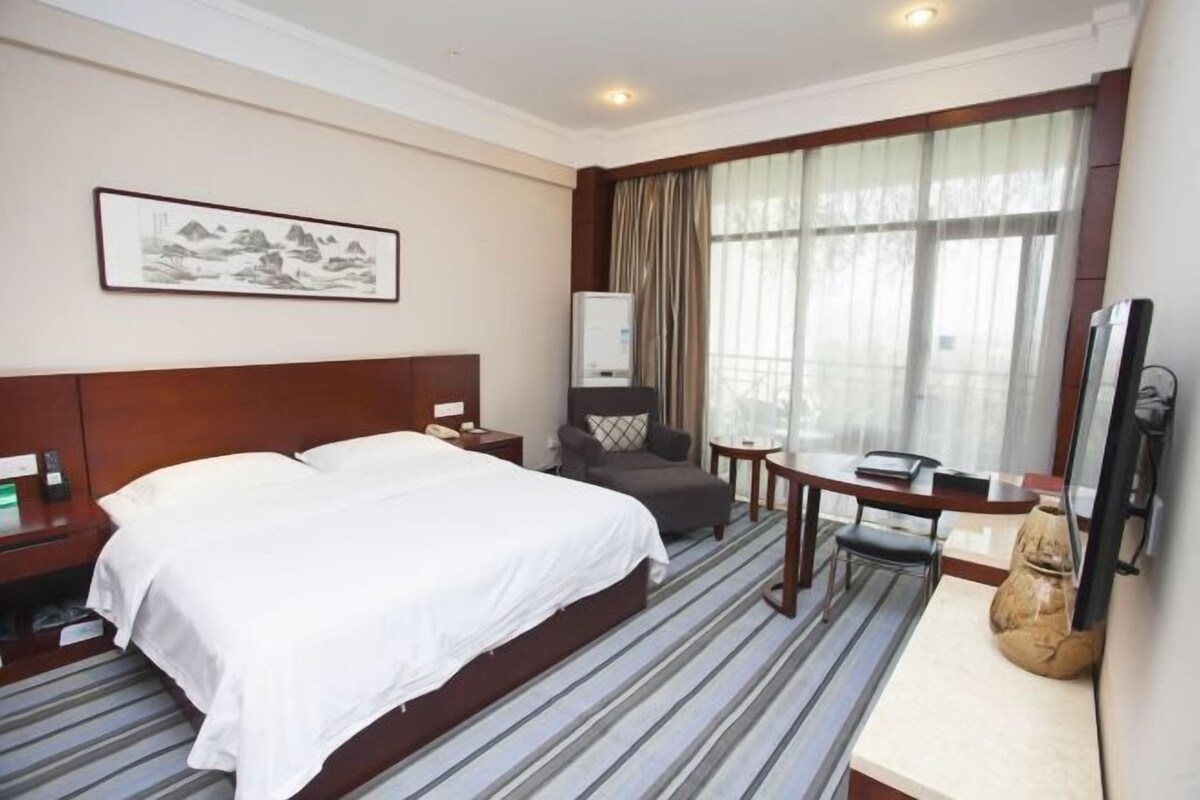 A hotel room with a bed, a desk, a chair, a television, and a window with curtains.