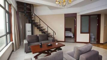 A modern living room with a sofa, a coffee table, a staircase, and a bed in the adjacent room.