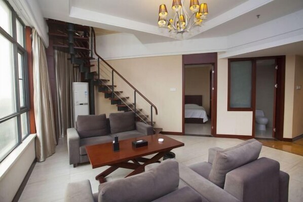 A modern living room with a sofa, a coffee table, a staircase, and a bed in the adjacent room. - Hequan Farm (Bengbu)