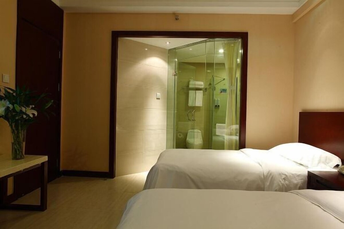 A hotel room with two beds, a glass-enclosed shower, and a wooden bench.