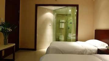 A hotel room with two beds, a glass-enclosed shower, and a wooden bench.
