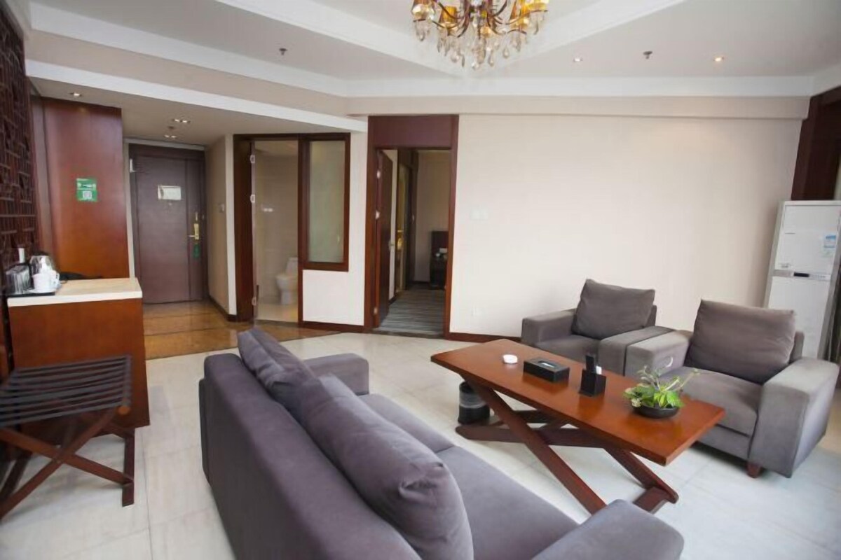 A modern hotel lobby with a reception desk, sofas, a wooden coffee table, and a chandelier.