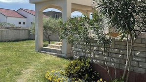 Un quartier résidentiel doté d’un patio couvert, d’un mur en pierre et d’une pelouse verdoyante parsemée de fleurs jaunes.