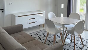 Un salon moderne et minimaliste, comprenant un canapé, une table à manger avec des chaises, un meuble blanc et un tapis à motifs.