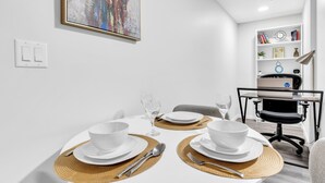 Un coin repas avec une table blanche dressée pour deux personnes, une bibliothèque et un ordinateur portable posé sur un bureau.