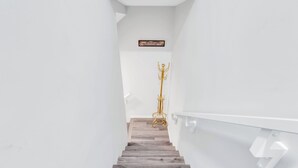 Un escalier avec des marches en bois et des murs blancs, un porte-manteau doré et une enseigne au-dessus de l’escalier.