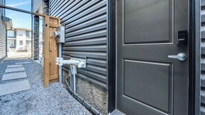 Un bâtiment moderne avec une façade sobre, une porte métallique fermée, un portail en bois et des tuyaux apparents.