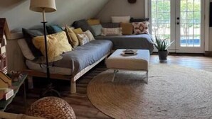 Un acogedor salón tipo loft con techo alto, ventilador de techo, una guitarra y un ventanal con vistas al exterior.