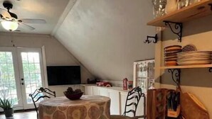 Una cocina con una mesa de comedor, sillas y un ventilador de techo. Se ve follaje verde a través de la ventana.