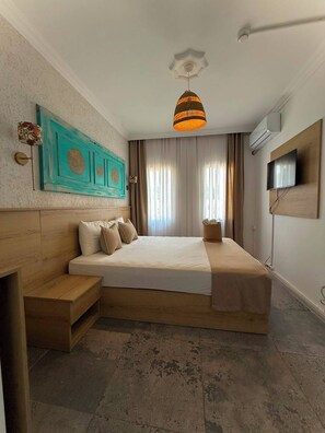 A hotel room with a large bed, a wooden bench, a wall-mounted TV, and a ceiling light fixture. - Bodrum Merkez Kumsal Pansiyon (Bodrum)