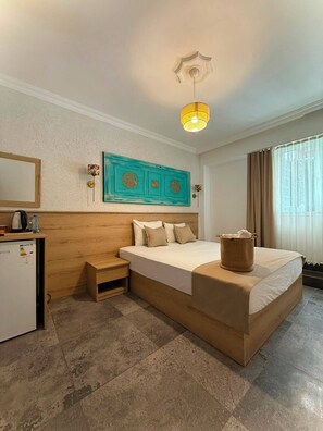 A hotel room with a bed, a desk, a small table, a wall-mounted artwork, and a window with curtains. - Bodrum Merkez Kumsal Pansiyon (Bodrum)