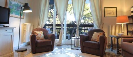 A living room with two brown armchairs, a glass coffee table, a television, and a framed picture on the wall.