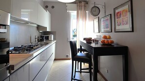 A modern kitchen with a gas stove, microwave, and sink. There is a dining table with chairs and a clock on the wall. - Provenzale Apartment, Lago di Garda, Jacuzzi (Desenzano Del Garda)