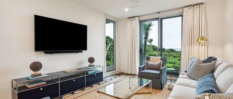 A modern living room with a flat-screen TV, a glass coffee table, and a sofa set.
