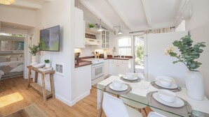 Uma cozinha moderna com armários brancos, uma mesa de jantar de vidro e uma mesa lateral de madeira.