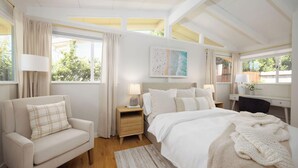 Quarto com cama, cadeira, escrivaninha e janela com cortinas.