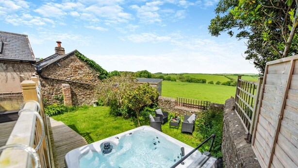 Ein Whirlpool in einem Garten mit Steinmauern, einer Holzterrasse und Blick auf die Landschaft.