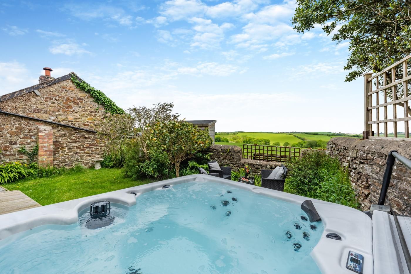 A hot tub in a garden with stone walls and a view of the countryside.