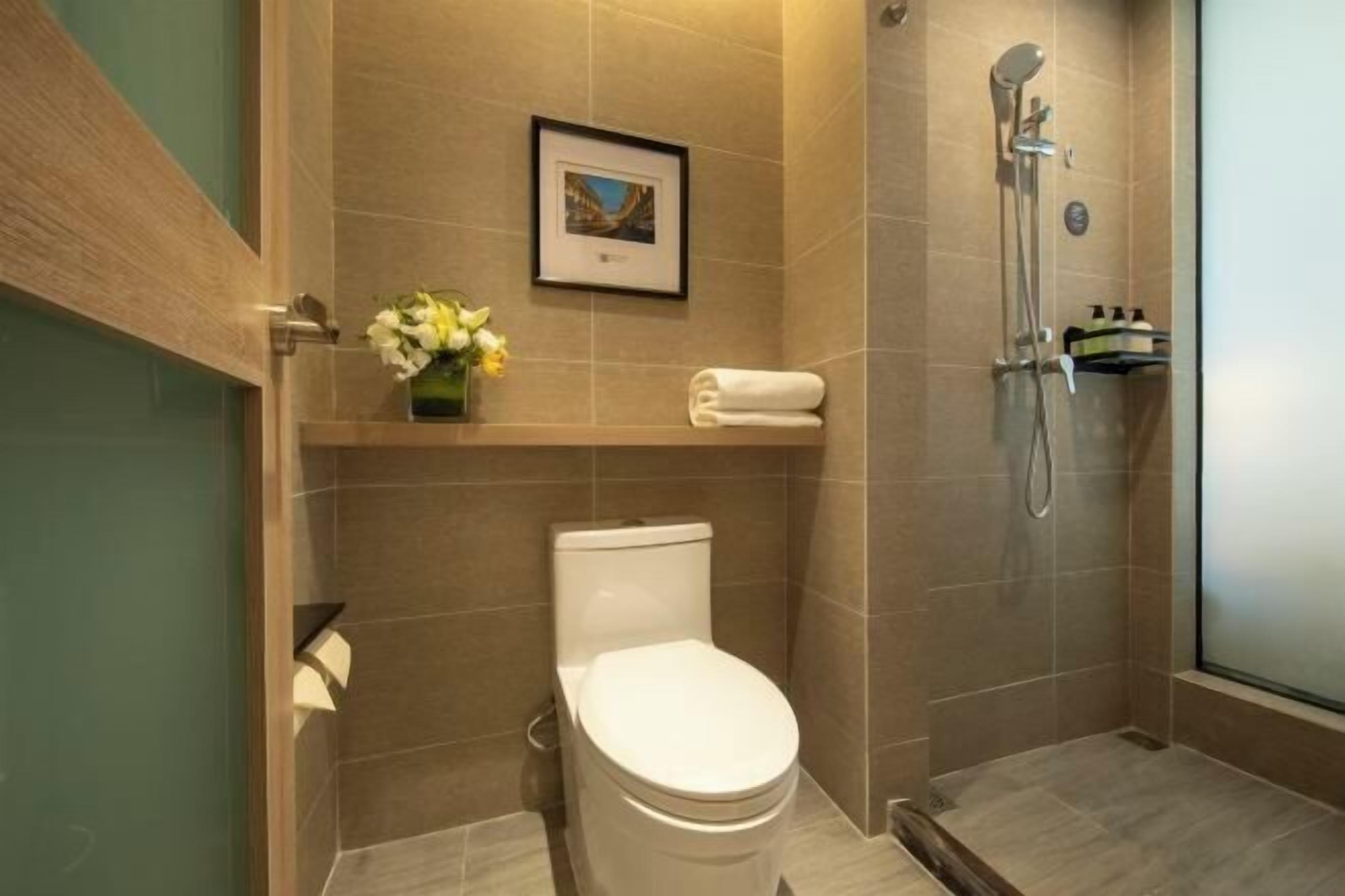 Ein Badezimmer mit Toilette, Dusche, einem gerahmten Bild an der Wand und einer Vase mit Blumen.
