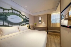 A hotel room with a bed, a desk, a chair, a TV, and a wall mural of a bridge over water. - Orange Hotel (Suzhou University East Ring Road Subway Station) (Suzhou)