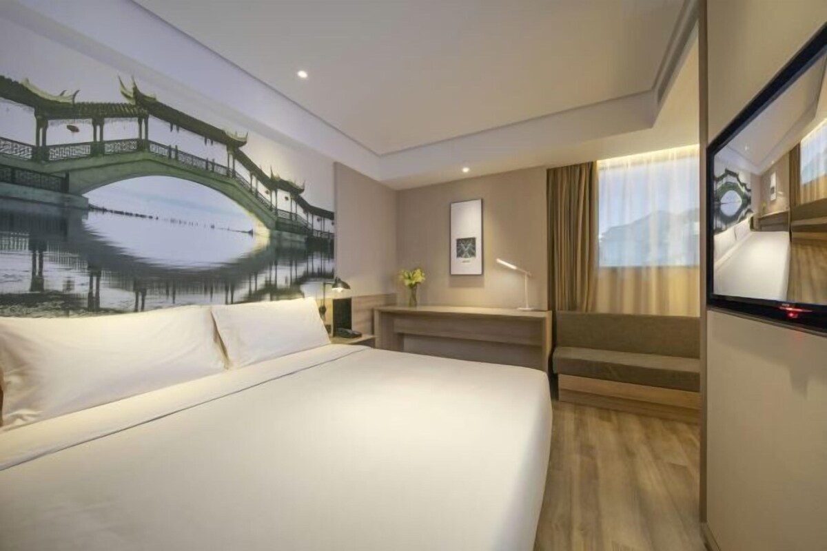 A hotel room with a large bed, a desk, a TV, and a mural of a bridge over water.
