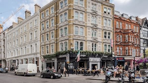 A historic building with multiple stories, featuring classic architectural details and a variety of storefronts on the ground floor. - Immaculate 2-bed Apartment in Prime Central London (London)