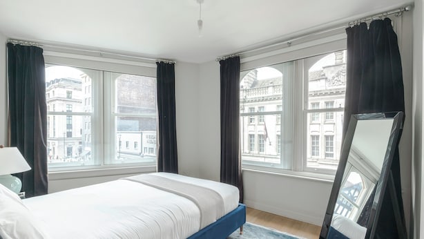A bedroom with a bed, large windows, a mirror, and a lamp. - Immaculate 2-bed Apartment in Prime Central London (London)