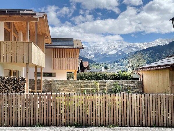 A modern house with a wooden deck, a stone wall, and a view of snow-capped mountains.