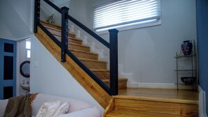 Una escalera con escalones de madera y barandillas negras, que lleva a una plataforma con pared blanca y una ventana con persianas.