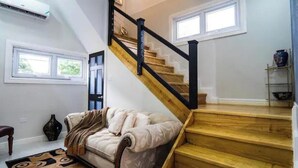 Una escalera con peldaños de madera y barandillas negras, un sofá color beige con una manta y un jarrón sobre una estantería.