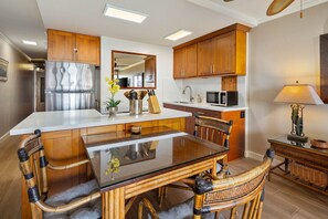 A modern kitchen with wooden cabinets, a stainless steel refrigerator, a glass dining table, and a microwave.