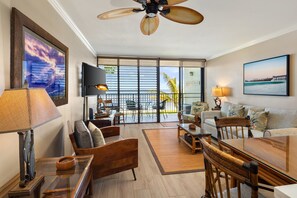 A spacious living area with a balcony, a television, and a ceiling fan. - Private Beachfront Retreat in Haleiwa (Haleiwa)