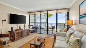 A living room with a TV, a sofa, a wooden console, and a balcony with a view. - Private Beachfront Retreat in Haleiwa (Haleiwa)