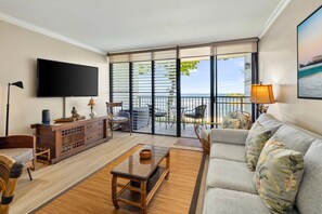 A living room with a TV, a sofa, a wooden console, and a balcony with a view. - Private Beachfront Retreat in Haleiwa (Haleiwa)