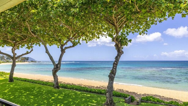 A beachfront property with a well-maintained lawn, a wooden deck, and a view of the ocean. - Private Beachfront Retreat in Haleiwa (Haleiwa)