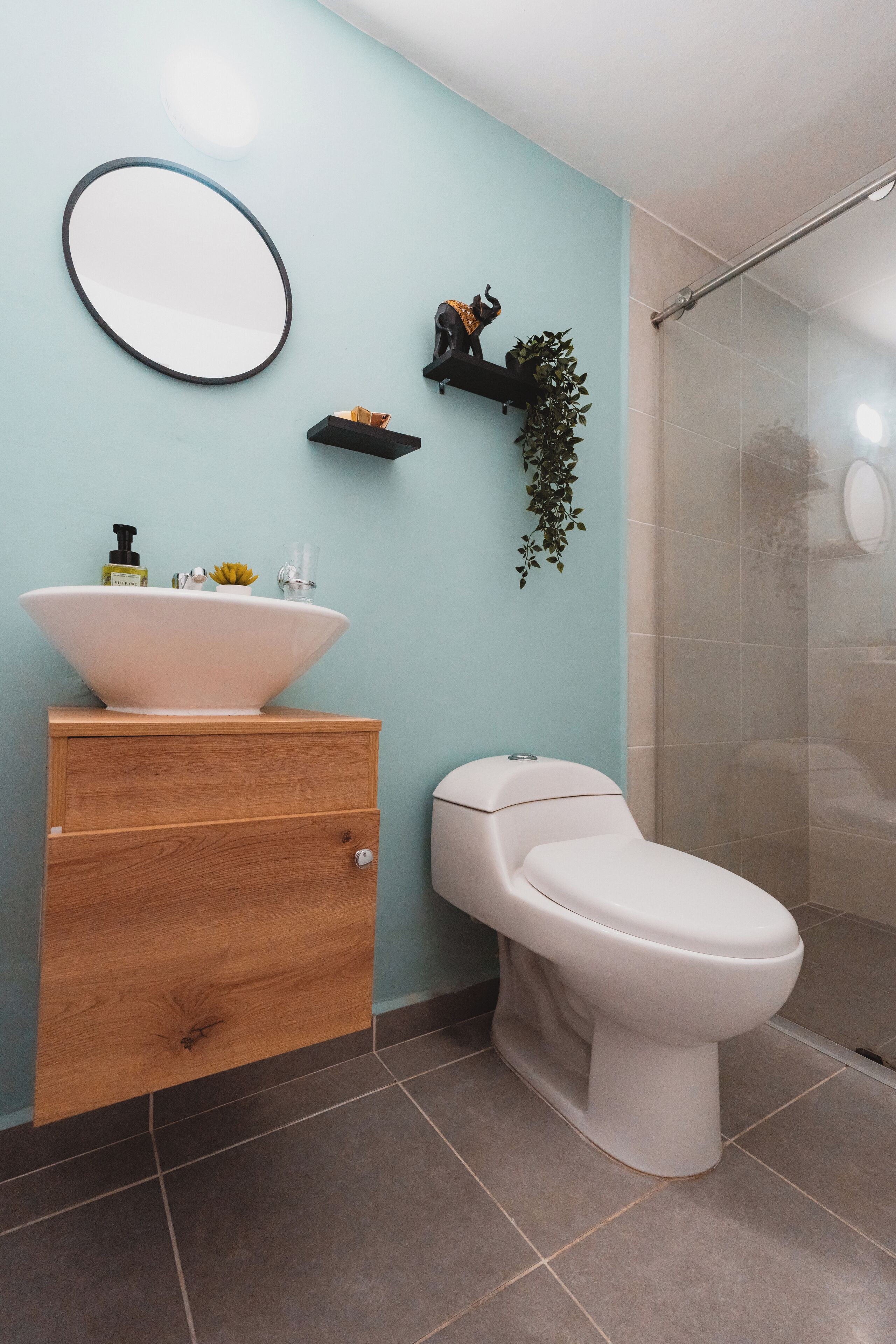 Un baño con inodoro blanco, espejo redondo y mueble de madera.