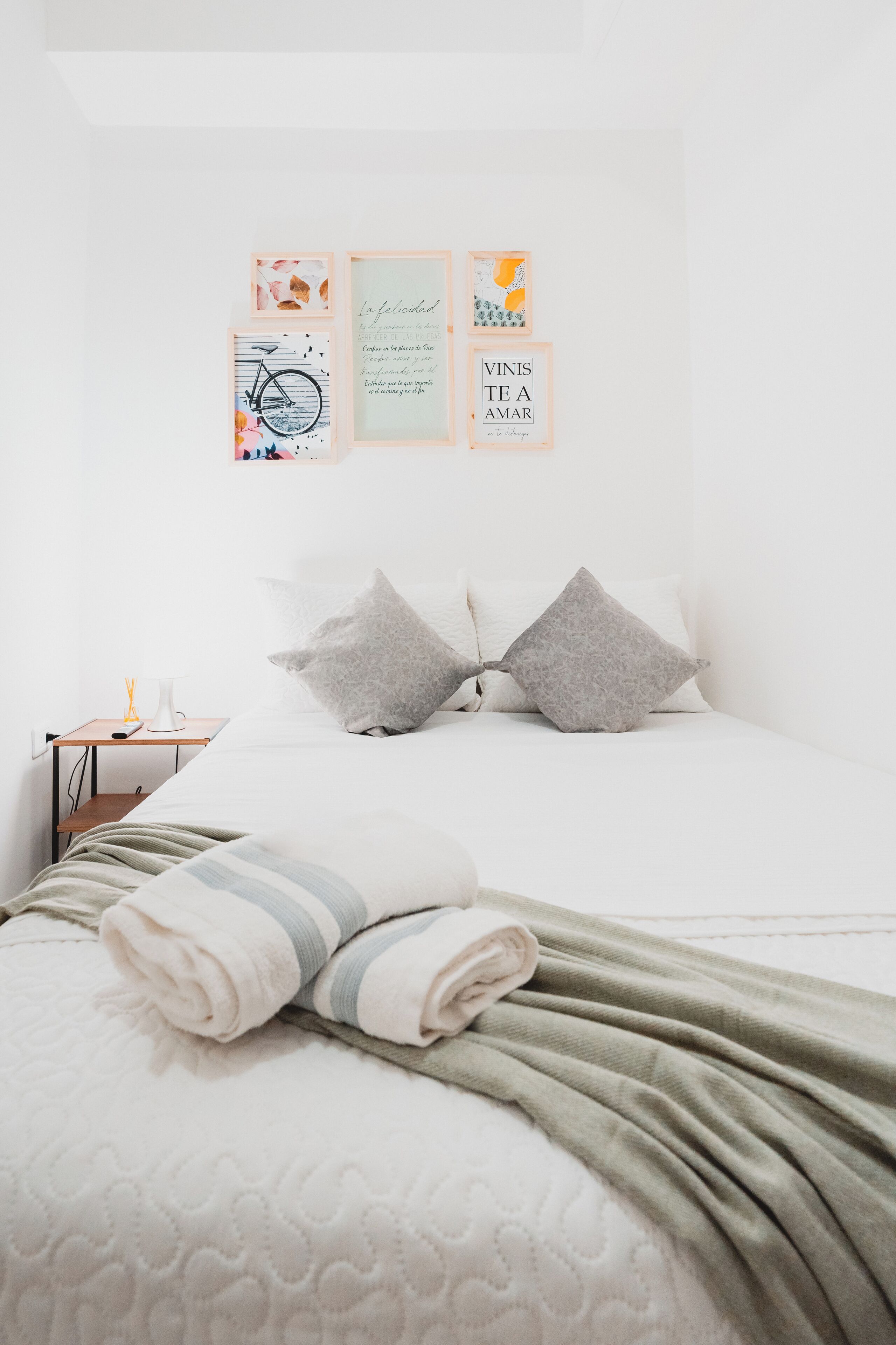 Un lit bien fait, avec des oreillers, une table de chevet avec une lampe et des œuvres d’art encadrées accrochées au mur.
