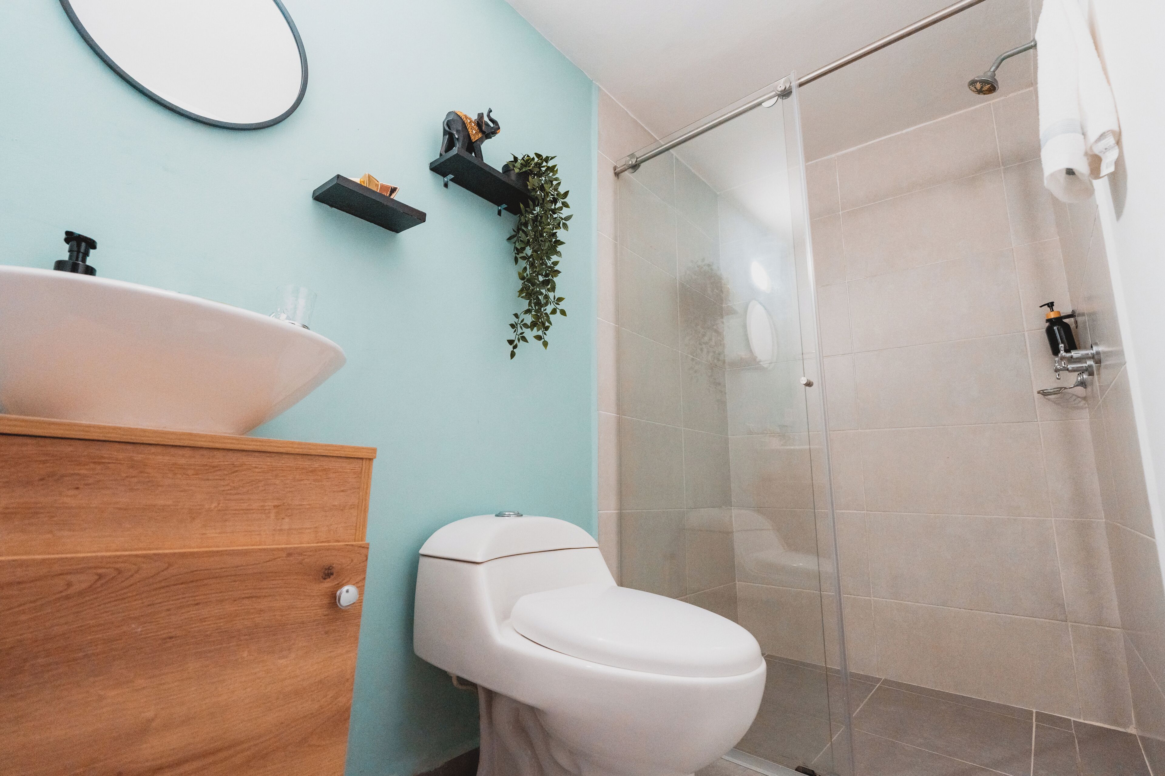 Un baño con tocador de madera, un lavabo blanco, inodoro, cabina de ducha de cristal y un estante con adornos.