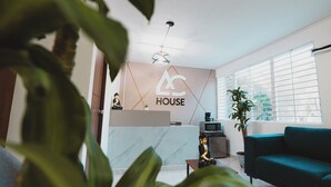 A modern living room with a sofa, a coffee table, and a TV. There is a wall with a logo and a ceiling fan. - AC - House Laureles - Self Checking (Medellín)
