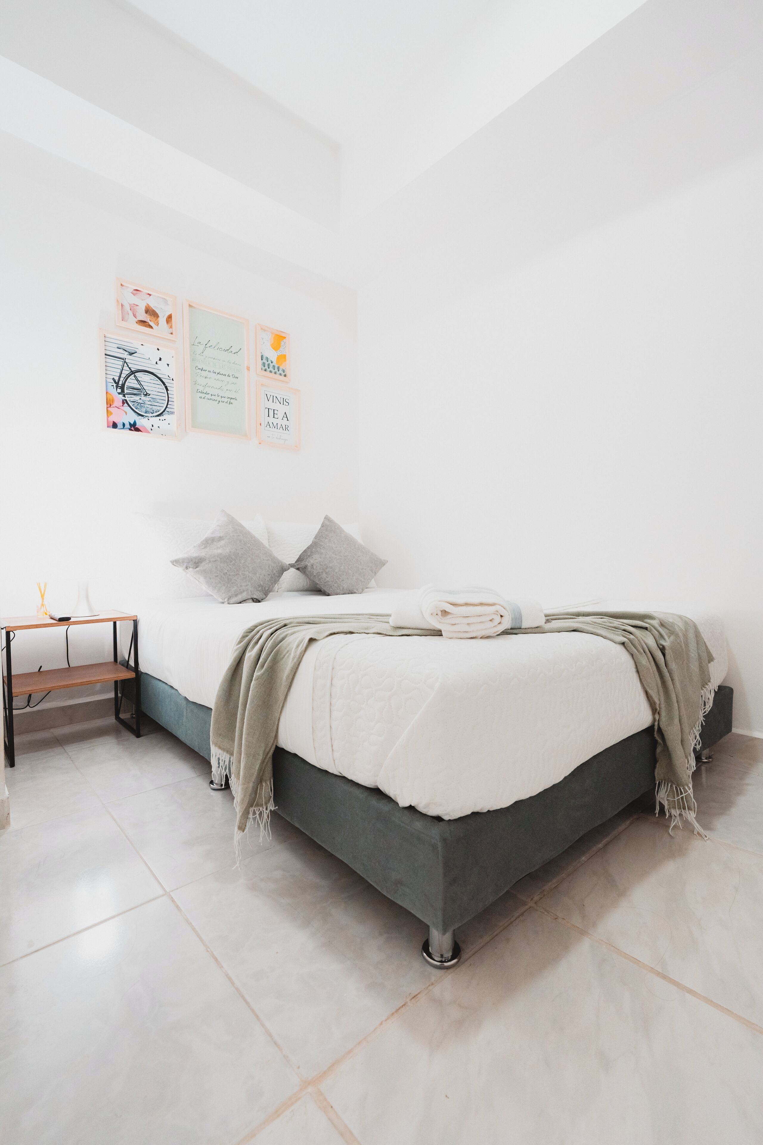 A minimalist bedroom with a bed, a bedside table, and wall art.