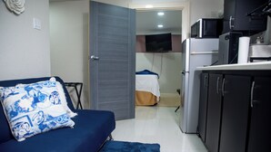 Un espace de vie compact comprenant un canapé, une petite kitchenette et un téléviseur fixé au mur.