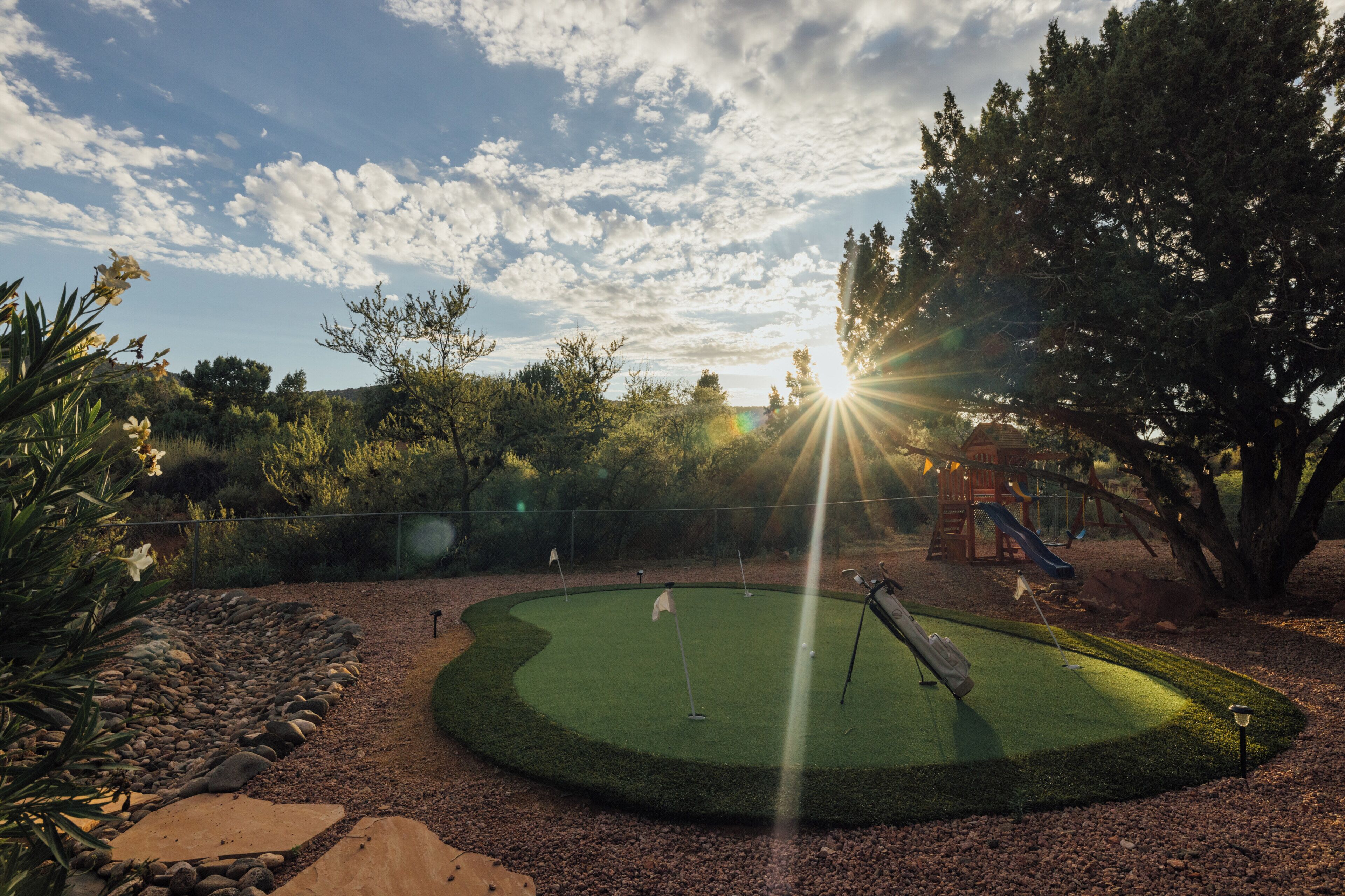 Un campo de golf con un putting green, árboles y un parque infantil.