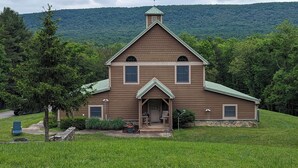A two-story house with a green roof, a front porch, and a stone foundation. - Private, light filled retreat space...
     with your own pickleball court! (Berkeley Springs)