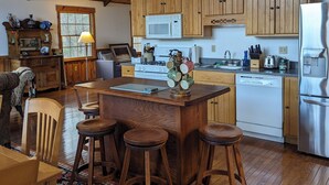 A cozy kitchen with wooden cabinets, a central island with stools, a patterned rug, and a rustic ceiling. - Private, light filled retreat space...
     with your own pickleball court! (Berkeley Springs)